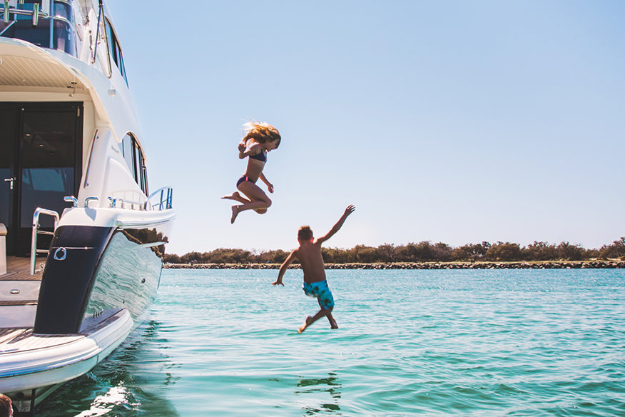 2 kids jumping from their yacht onto the water
