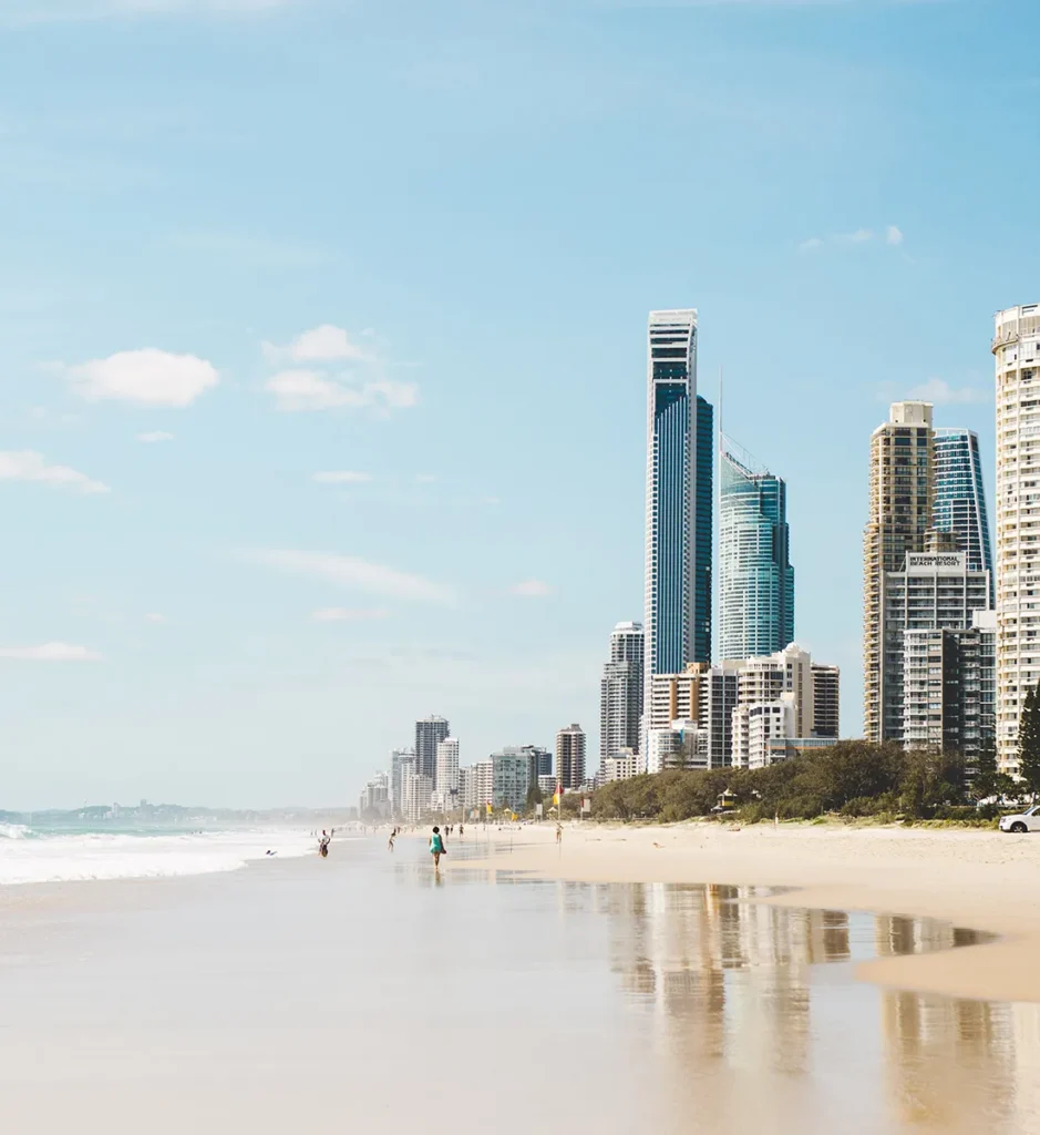 Surfers enjoying the Gold Coast coastline with the city skyline in the distance, showcasing the lifestyle of living on the Gold Coast.
